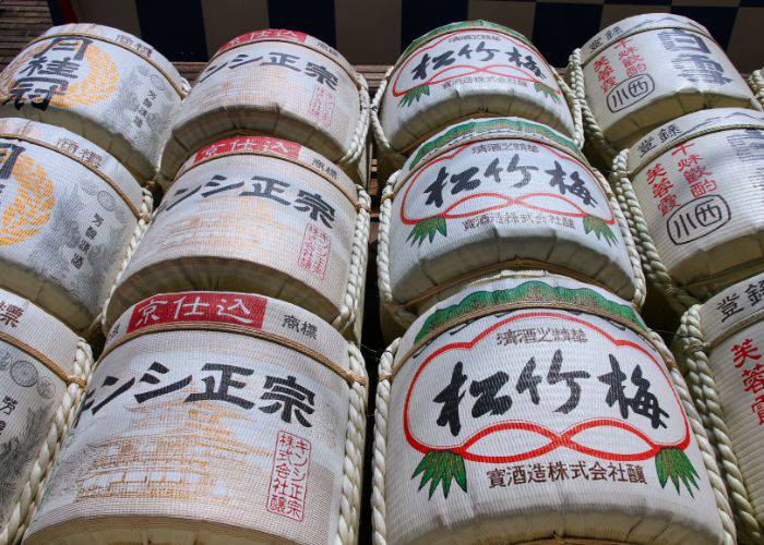 Looking up at stacked sake barrels, covered in brand names and logos.